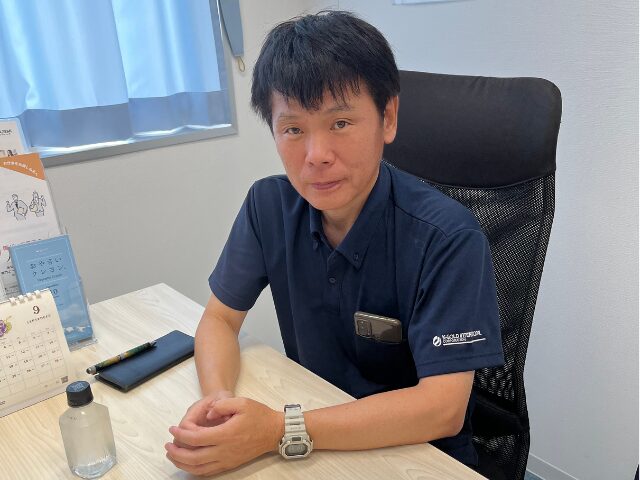 机の前に座る斉藤部長の写真